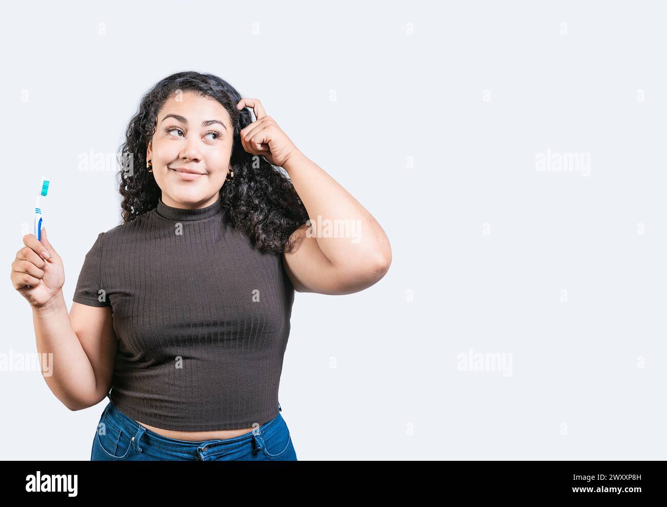 Bella donna con uno spazzolino isolato. Ragazza premurosa che tiene in mano lo spazzolino e guarda in alto in modo isolato Foto Stock