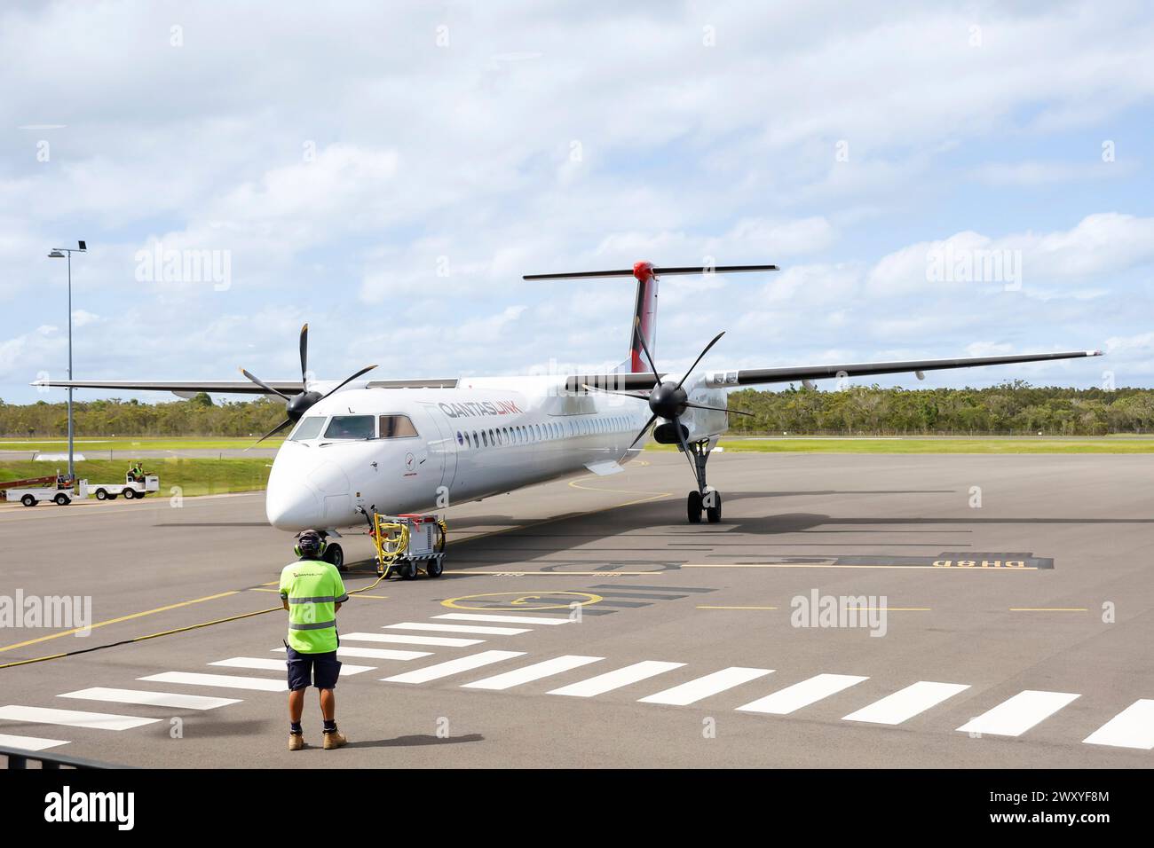 Addetto ai servizi che guarda l'aereo regionale turboelica Qantaslink Dash 8 sulla pista dell'aeroporto di Hervey Bay, Queensland, Australia Foto Stock