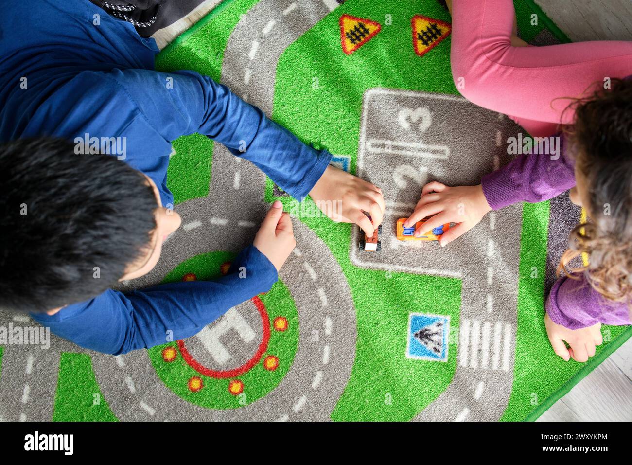 Da sopra due bambini, un ragazzo e una ragazza, si impegnano in un gioco fantasioso con piccole macchinine giocattolo su un tappeto vibrante Foto Stock