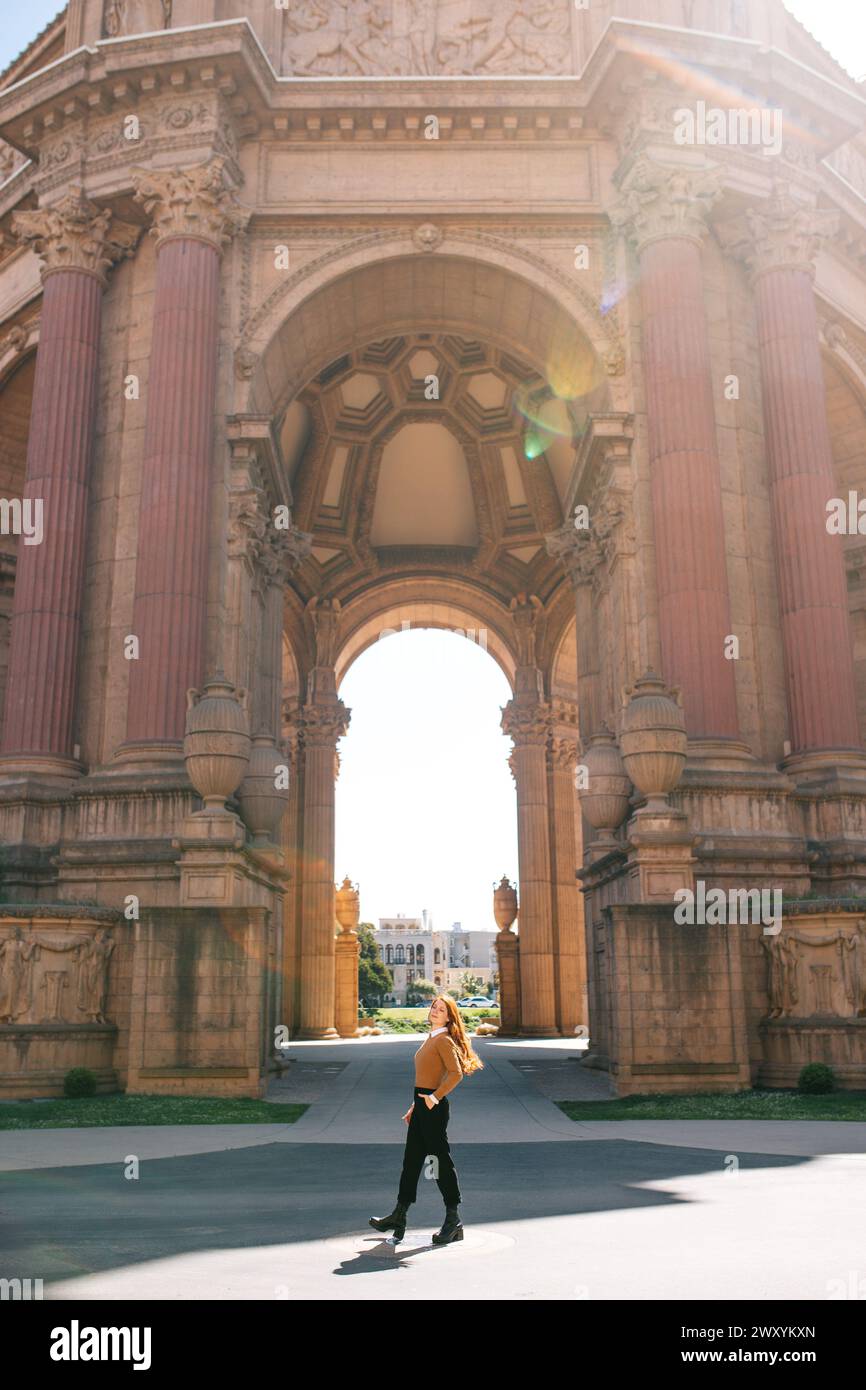 Una donna con un abbigliamento informale cammina con sicurezza attraverso i giardini del Palazzo delle Belle Arti, crogiolandosi al sole primaverile di San Francisco Foto Stock