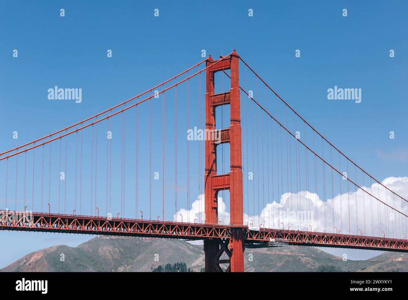 L'iconico Golden Gate Bridge si erge alto sotto il cielo blu brillante della primavera, completato da soffici nuvole bianche e colline ondulate Foto Stock