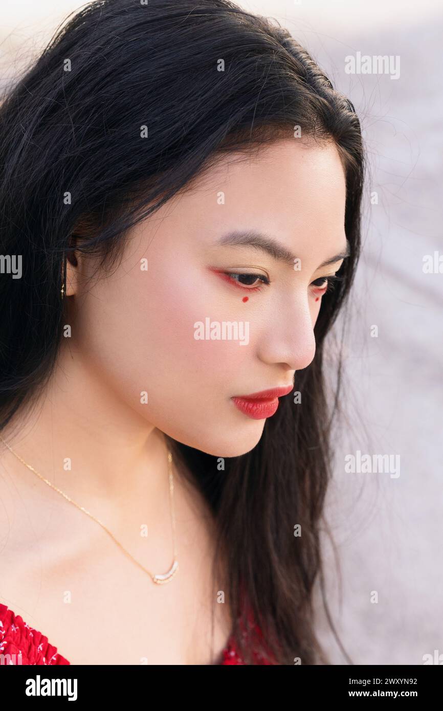 Un ritratto ravvicinato di una giovane donna che guarda verso il basso, catturato con una luce naturale soffusa, che mette in risalto le sue caratteristiche e la sua bellezza culturale Foto Stock