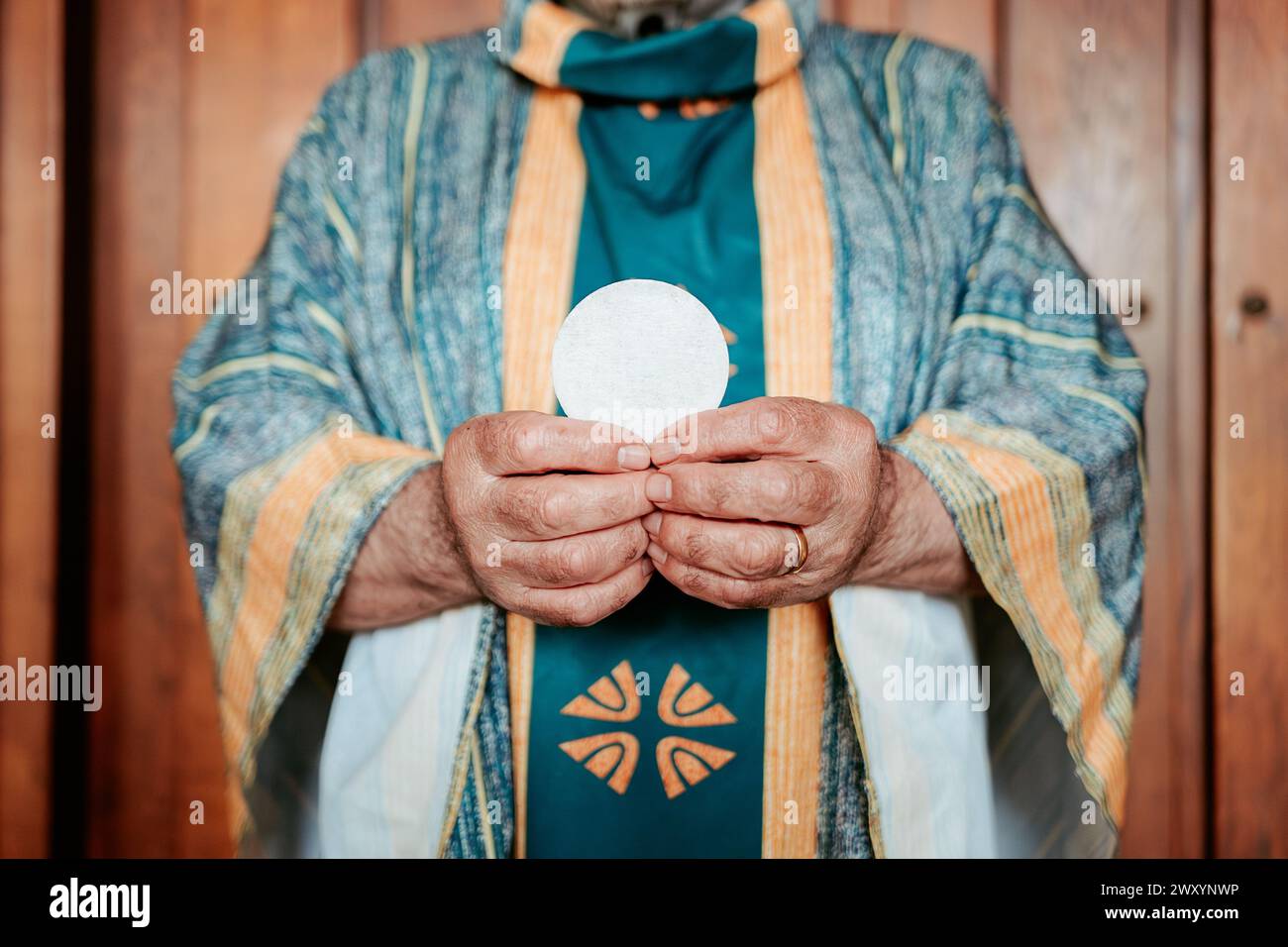 Primo piano delle mani anonime del sacerdote che presentano l'ospite eucaristico, un simbolo sacro nella Santa Comunione cristiana Foto Stock