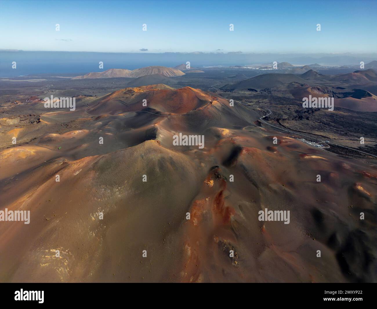 Accattivante drone sorvolò l'unico terreno vulcanico di Lanzarote, mostrando un arazzo di ricche tonalità di terra sotto un cielo azzurro Foto Stock
