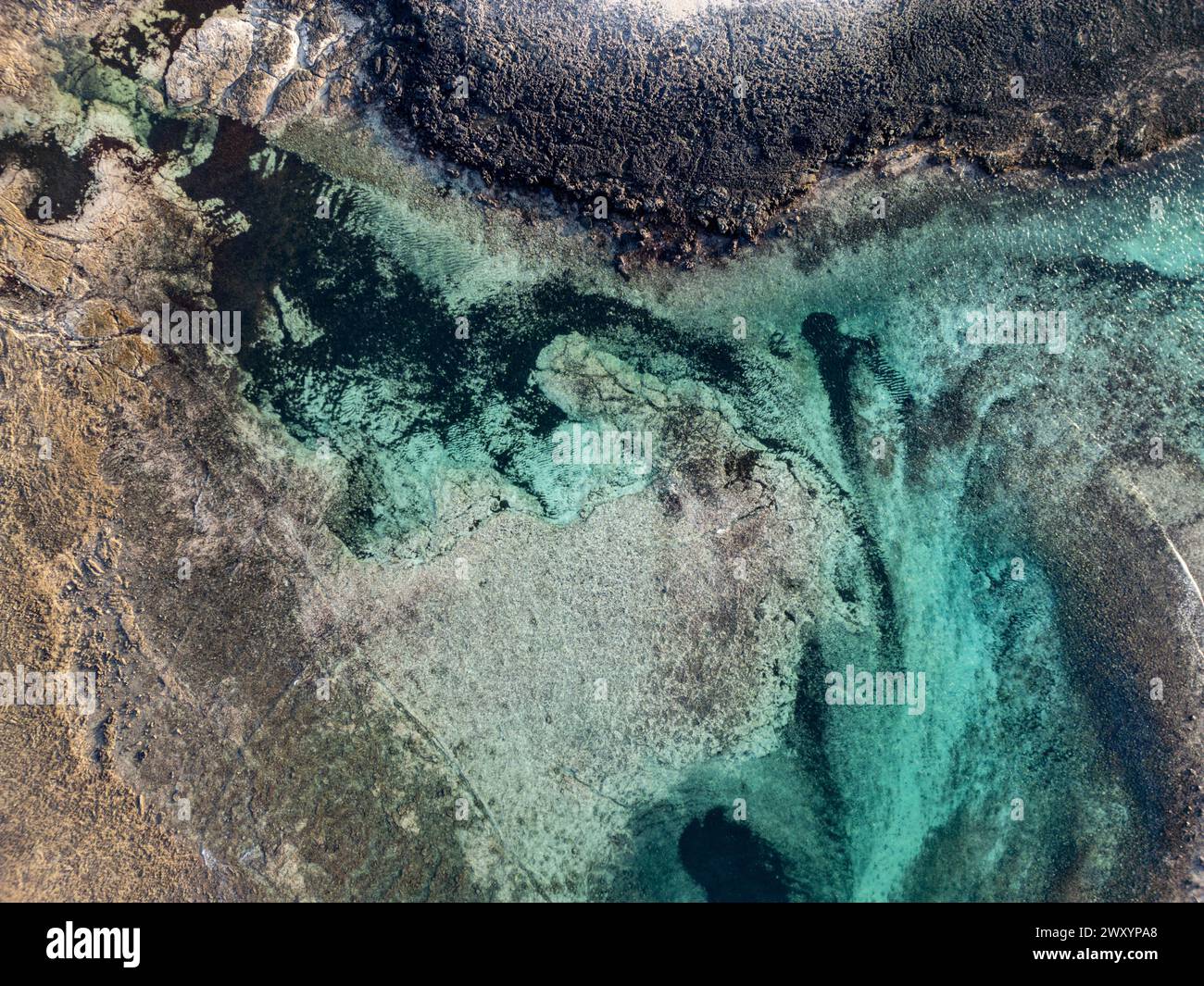 Una foto dall'alto cattura l'incredibile contrasto tra la costa frastagliata e le acque marine trasparenti e acquatiche Foto Stock