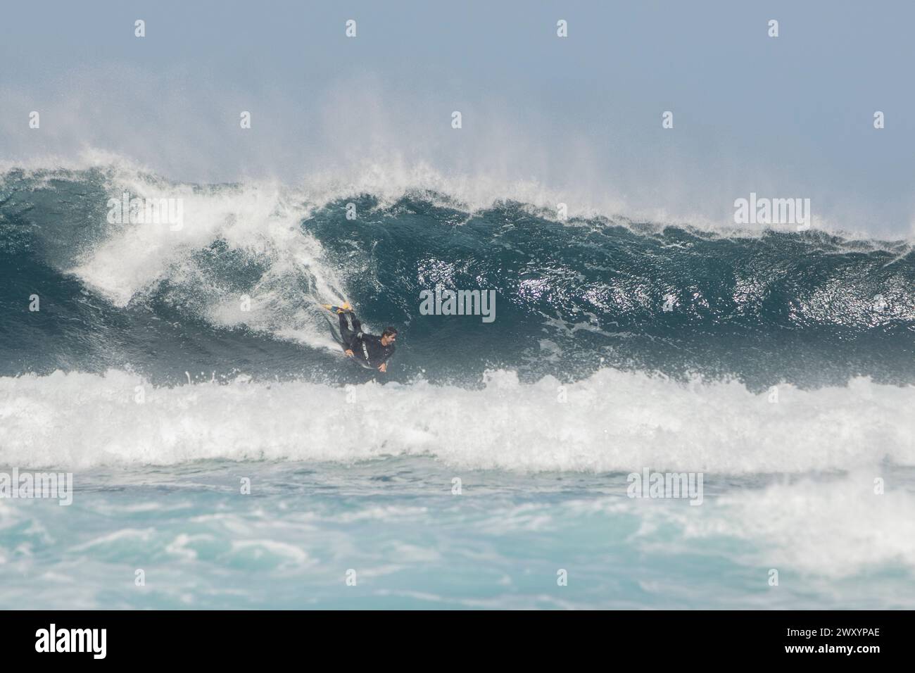 "Un intrepido surfista cattura un'onda torreggiante, con spruzzi di mare che nebulizzano l'aria, mostrando il brivido del surf." Foto Stock