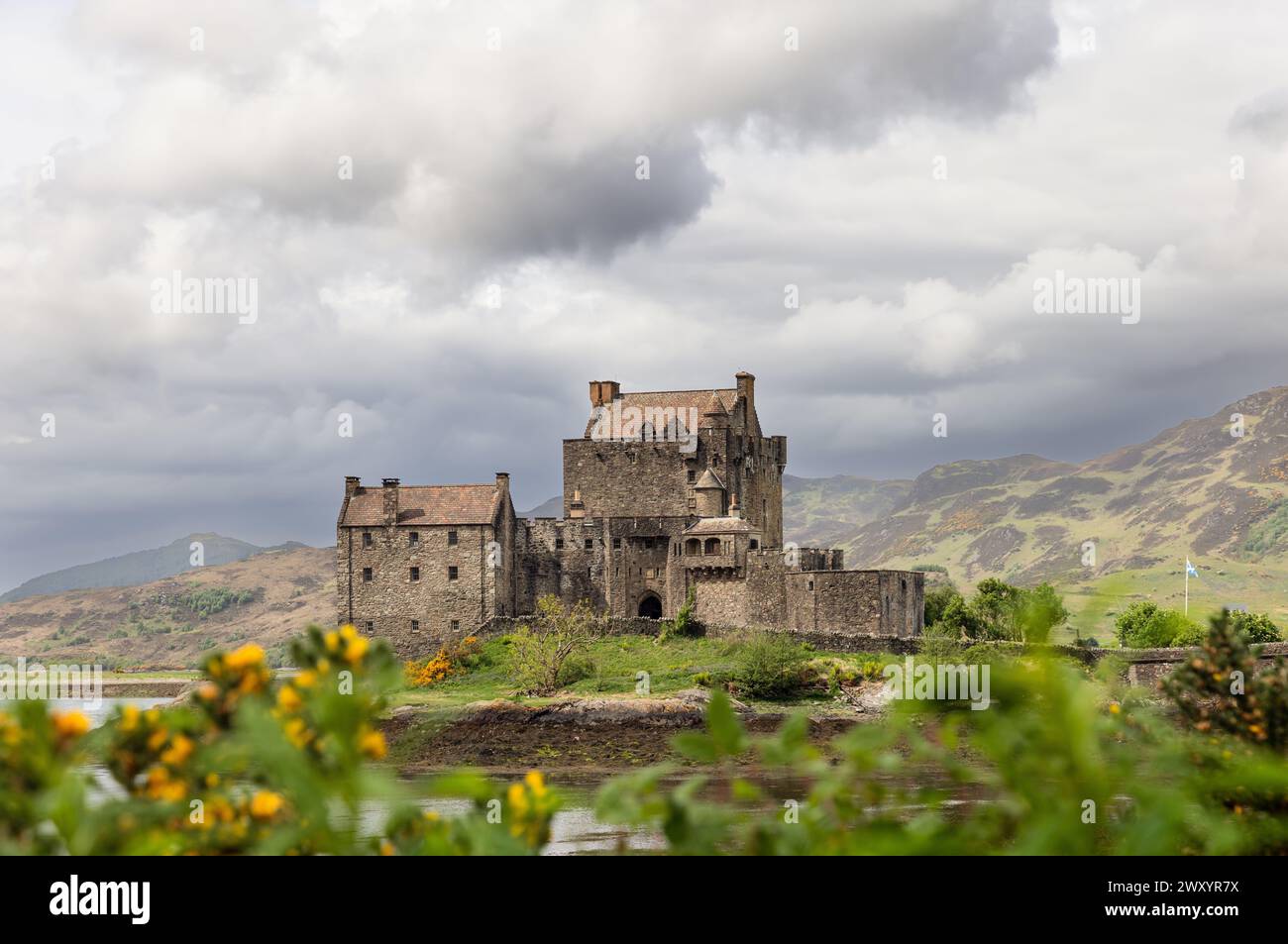 Il castello di Eilean Donan, simbolo della storia scozzese, è circondato da una flora vibrante e da un lago riflettente con gli altipiani che si innalzano dolcemente Foto Stock