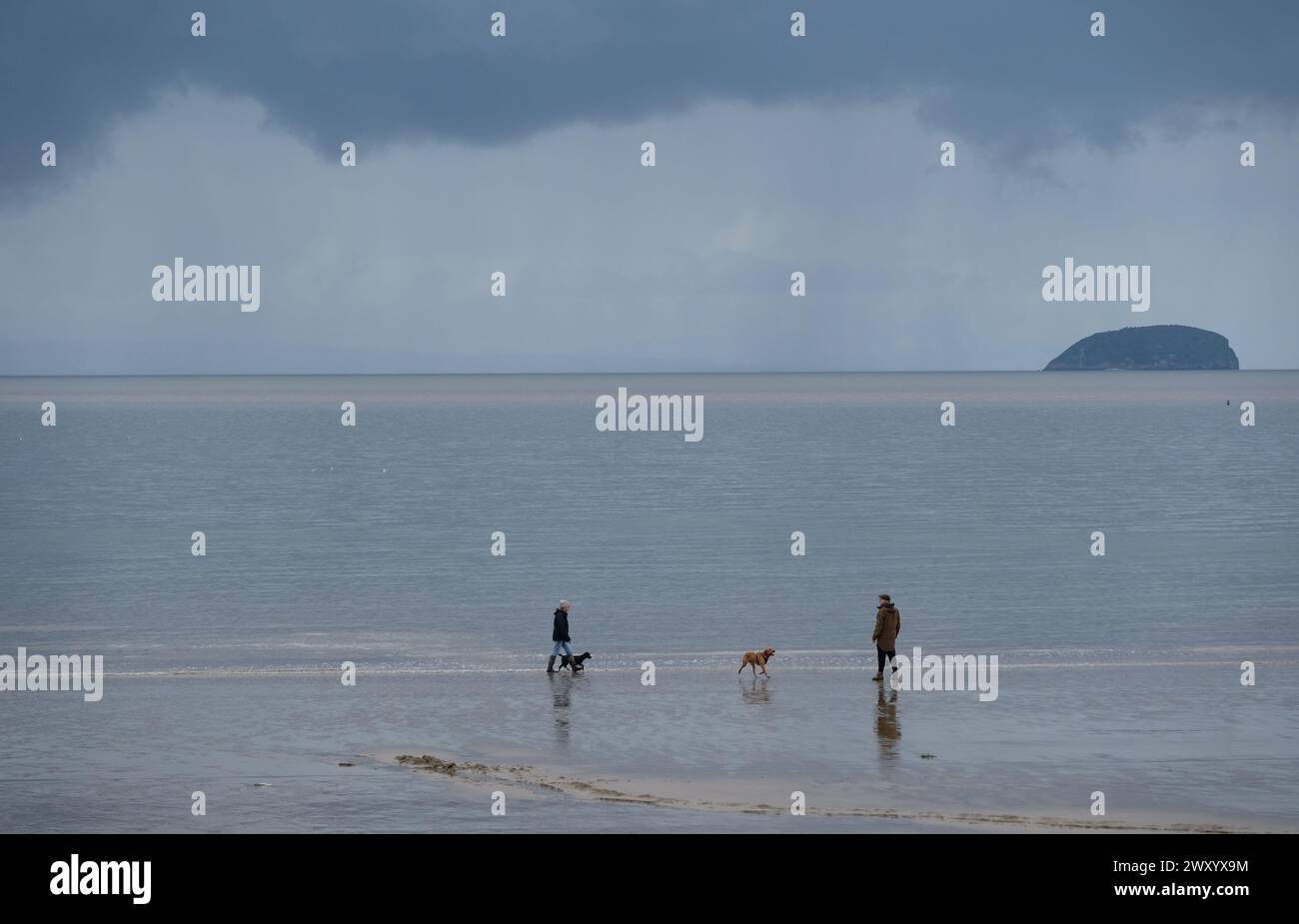 Persone che camminano su una spiaggia fredda, bagnata, ventosa e piovosa. Foto Stock