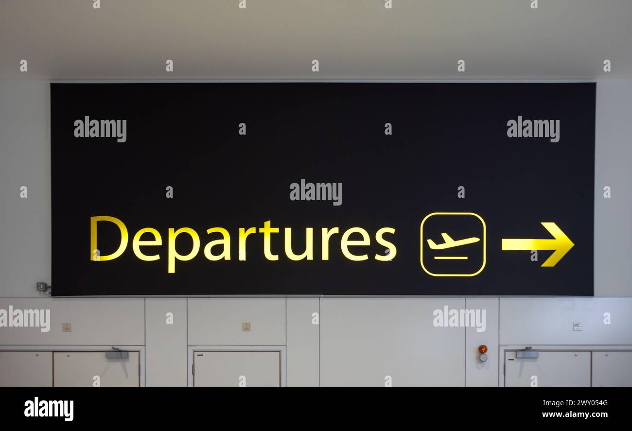 Un cartello giallo illuminato "Partenze" con una freccia e un'immagine di un aereo che decolla a North Terminial, Aeroporto di Gatwick, Londra, Regno Unito. Foto Stock