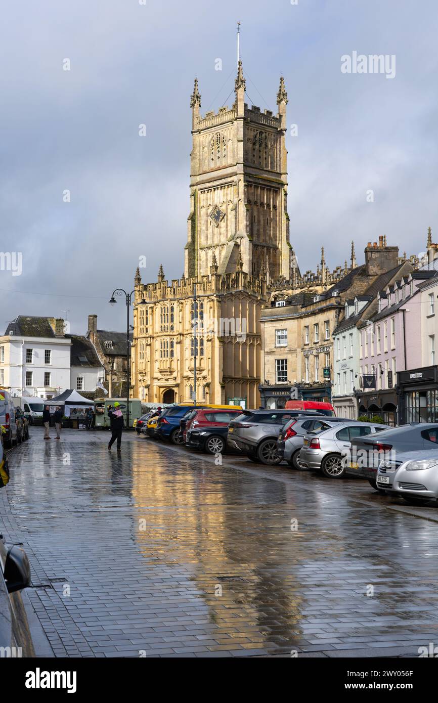 La chiesa medievale di San Giovanni Battista e il portico meridionale, con architettura gotica perpendicolare, si riflettono nelle pozzanghere. Cirencester, Regno Unito Foto Stock