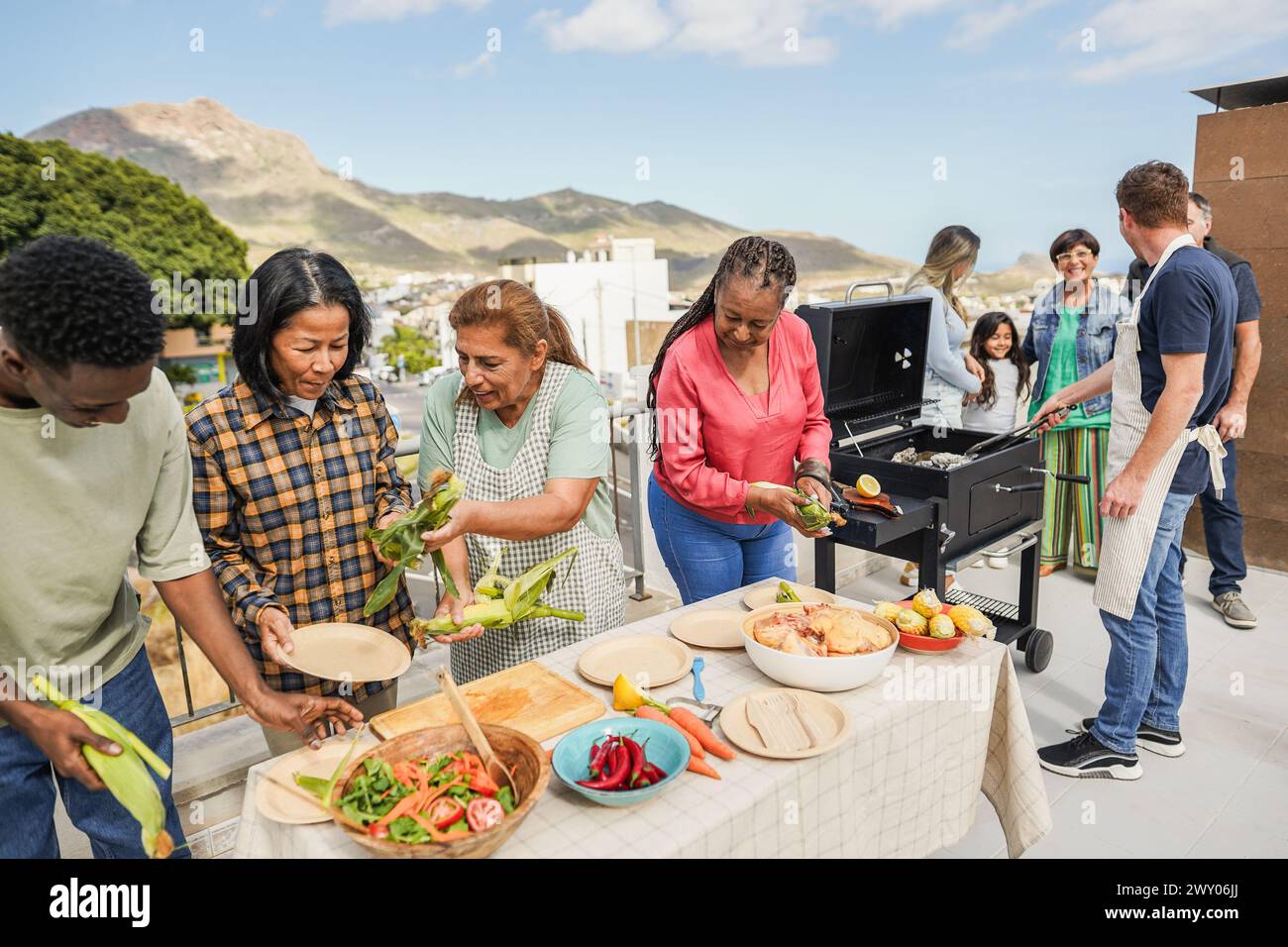 Persone multigenerazionali che fanno barbecue sul tetto di casa - amici multirazziali che si divertono a mangiare e cucinare insieme durante il giorno del fine settimana - estate e.. Foto Stock