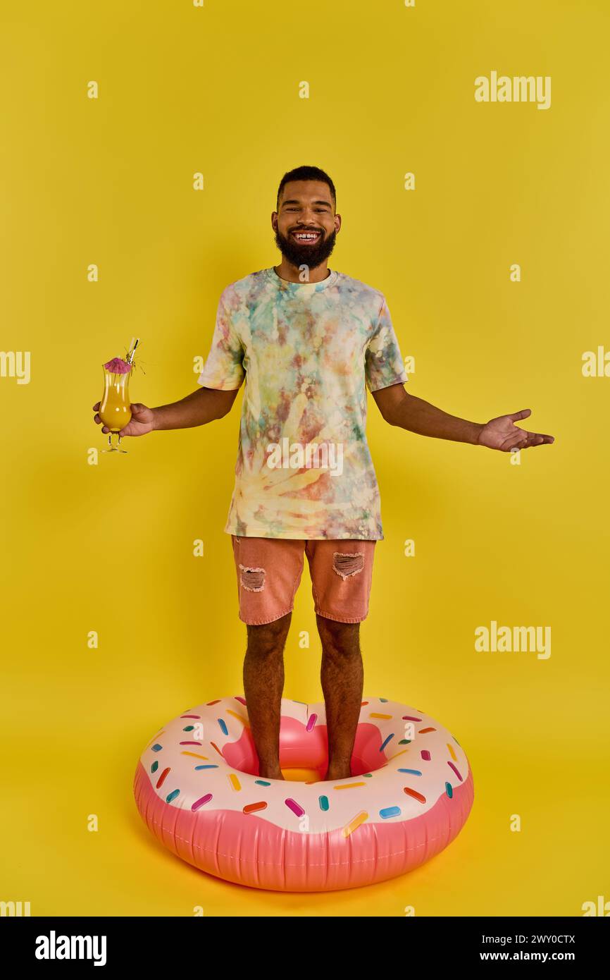 Un uomo si bilancia con sicurezza su una ciambella gigante, bevi in mano, in una scena surreale e stravagante. Foto Stock