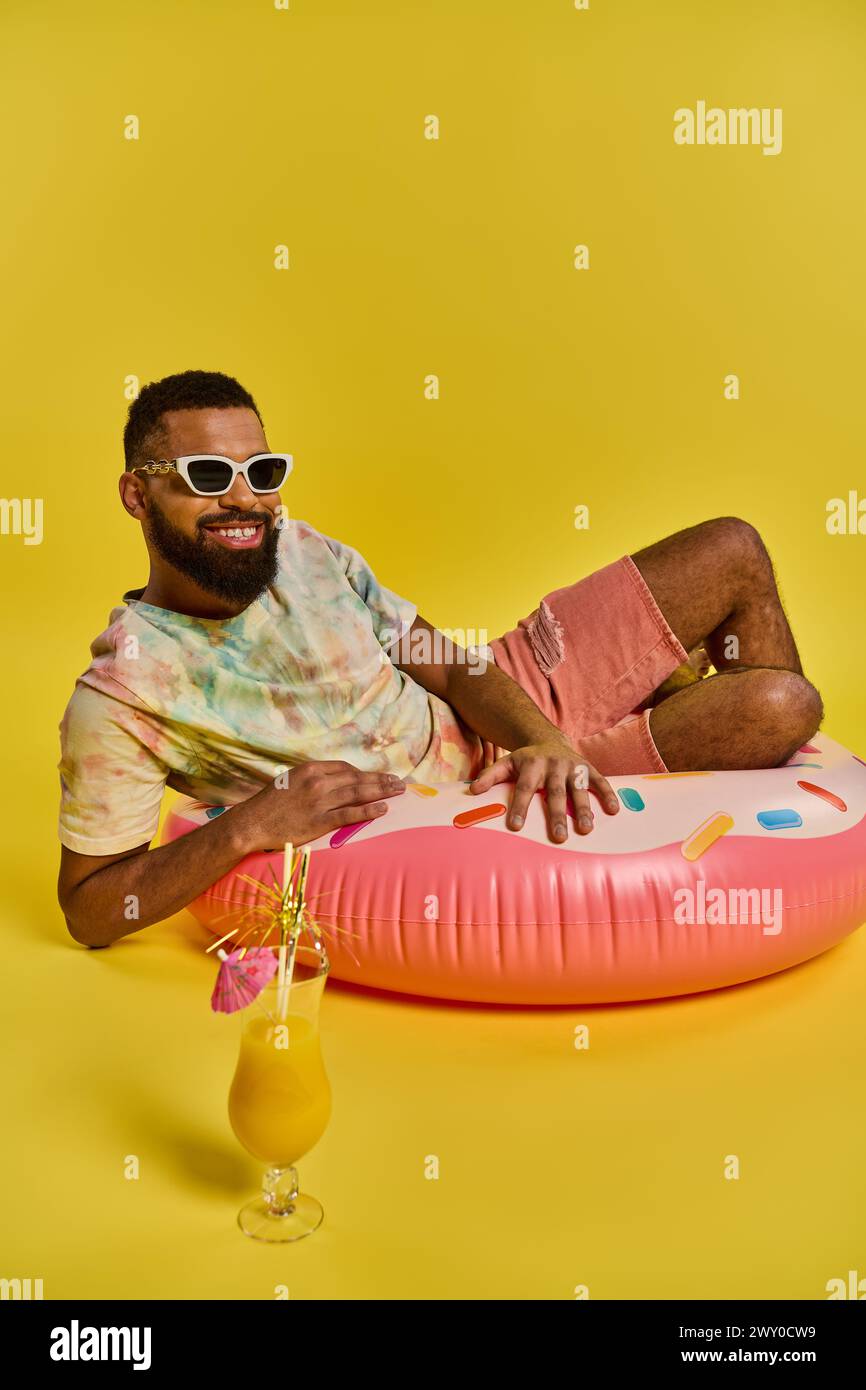 Un uomo si rilassa su un galleggiante gonfiabile, tenendo in mano un drink, galleggiando senza sforzo sulle acque serene sotto il sole. Foto Stock