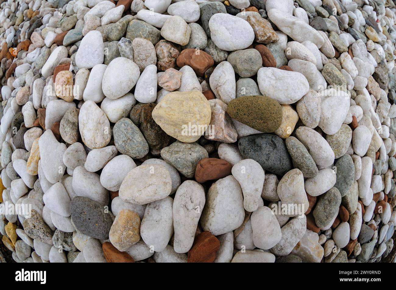 Un assortimento di ciottoli arrotondati in vari colori forma un design a spirale su terreno sabbioso. Foto Stock