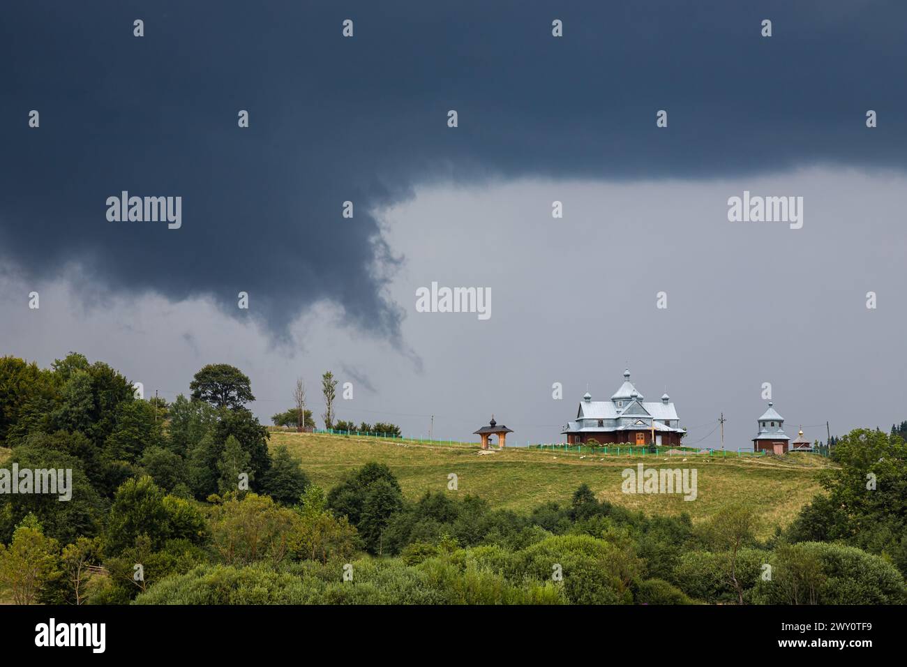 Nuvole tempesta, cielo minaccioso, collina e chiesa, alberi verdi prima della pioggia. Foto Stock