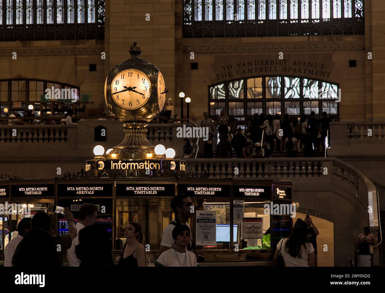 New York, NY - 7 agosto 2023: I pendolari passano l'orologio al Grand Central Terminal sulla 42a strada a Manhattan. Stazione ferroviaria urbana trafficata. Foto Stock