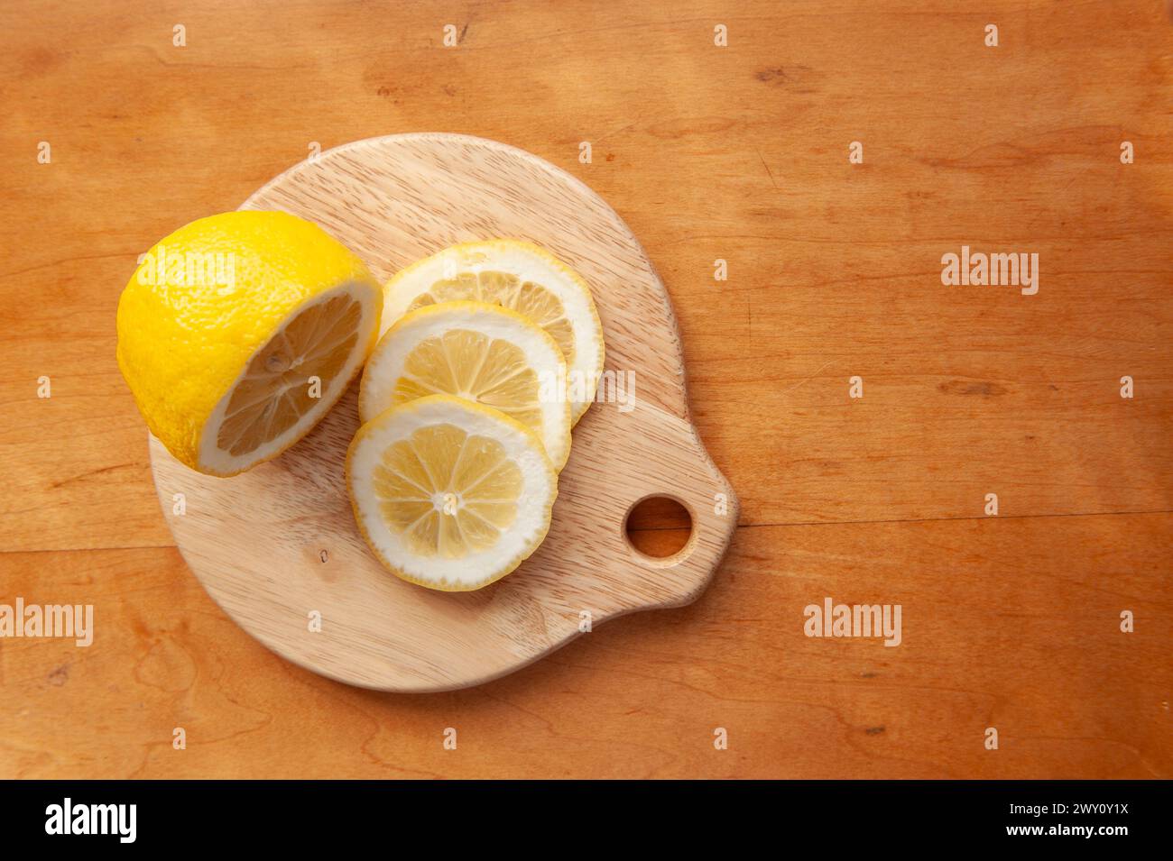 Mezzo limone e fette di limone fresco su un tagliere rotondo di legno Foto Stock