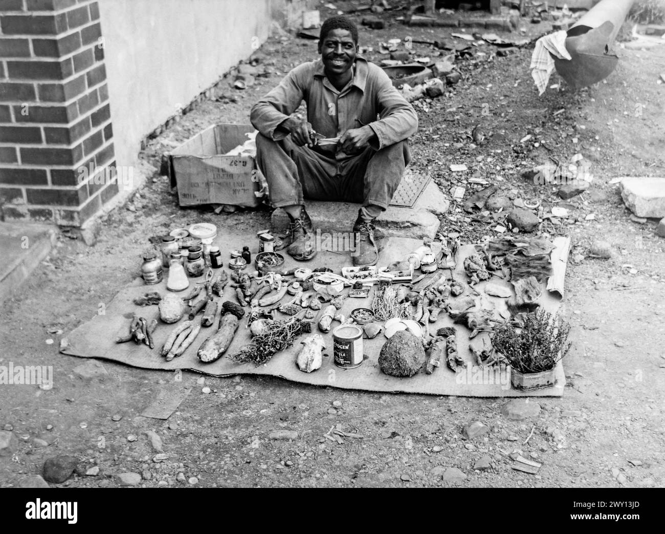 Uomo per strada che vende un assortimento di radici, erbe e altre cose a/vicino Ndola, Rhodesia settentrionale (ora Zambia) c1956 Foto Stock