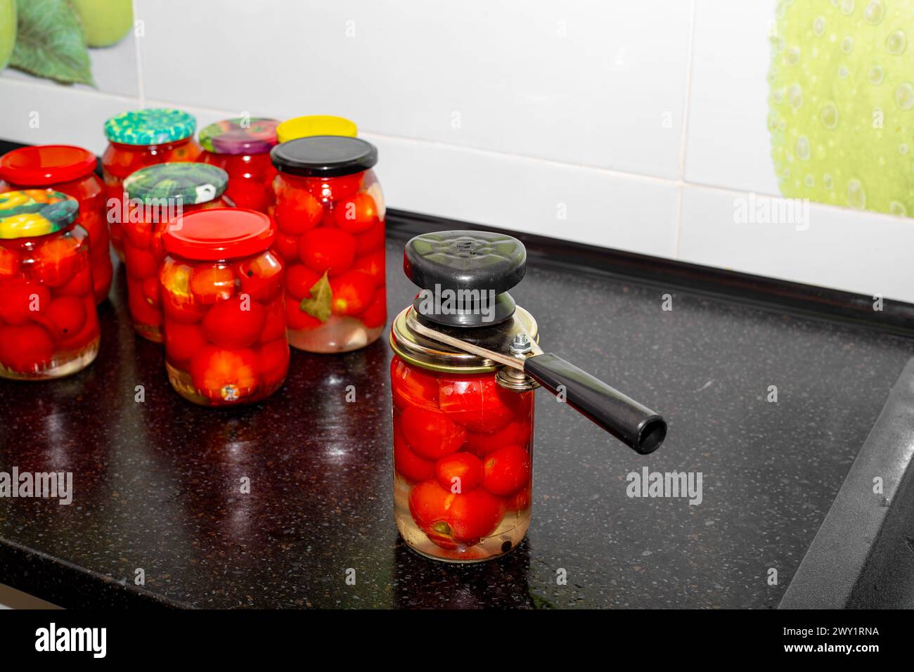 Conserve di pomodori. Vasetti di vetro pieni di pomodori rossi maturi immersi in salamoia. Avvitare i coperchi su un recipiente con una macchina per cucire. Foto Stock