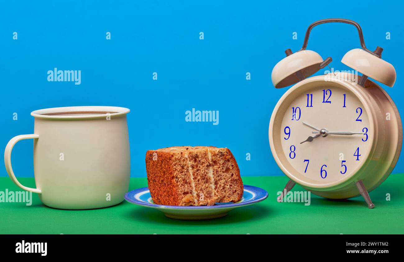 Concetto di tempo del caffè con tazza di caffè, sveglia e un pezzo di torta con sfondo colorato. Foto Stock