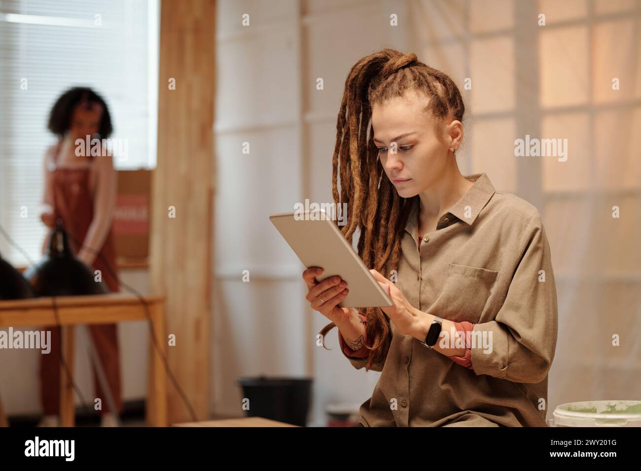 Giovane donna seria con dreadlock che utilizza un tablet mentre raccoglie informazioni online sul rinnovo della posizione di fronte alla fotocamera Foto Stock