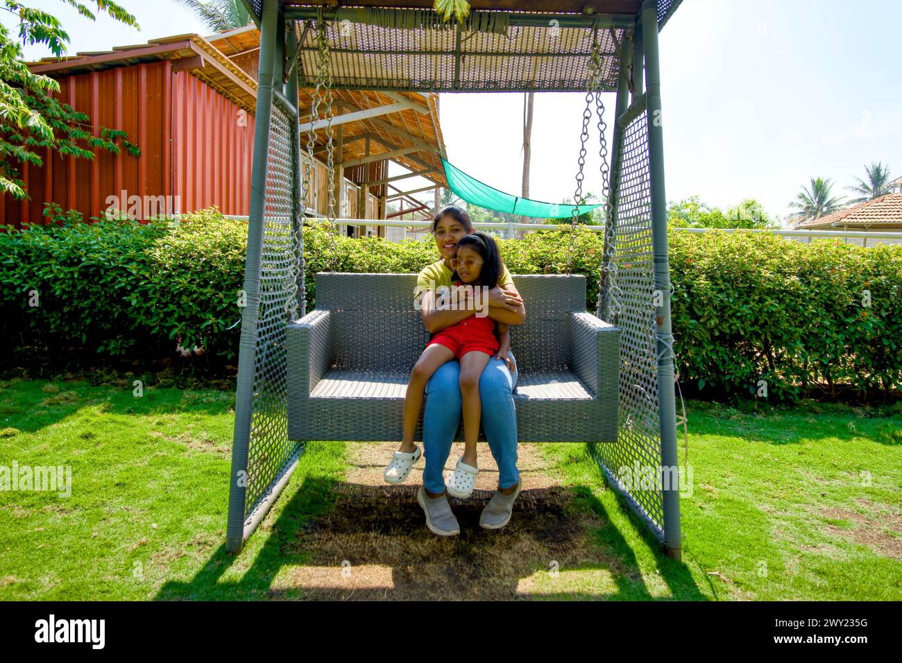 Una scena deliziosa che cattura una madre e sua figlia che si godono un momento spensierato su un'altalena in un giardino vivace Foto Stock