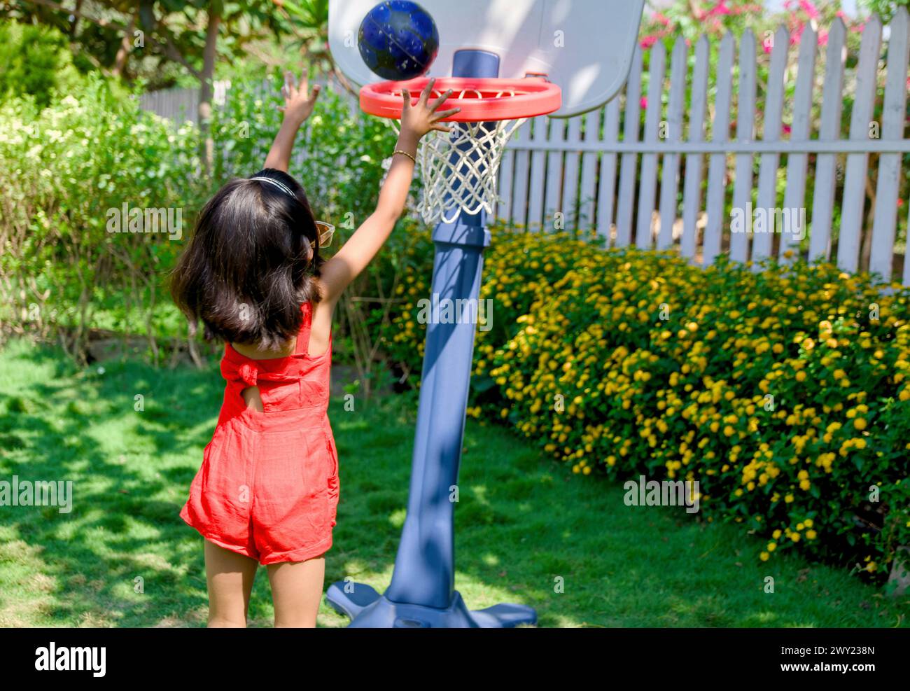 Una bambina con un'espressione decisa bagna una pallacanestro in una giornata di sole nel suo cortile Foto Stock