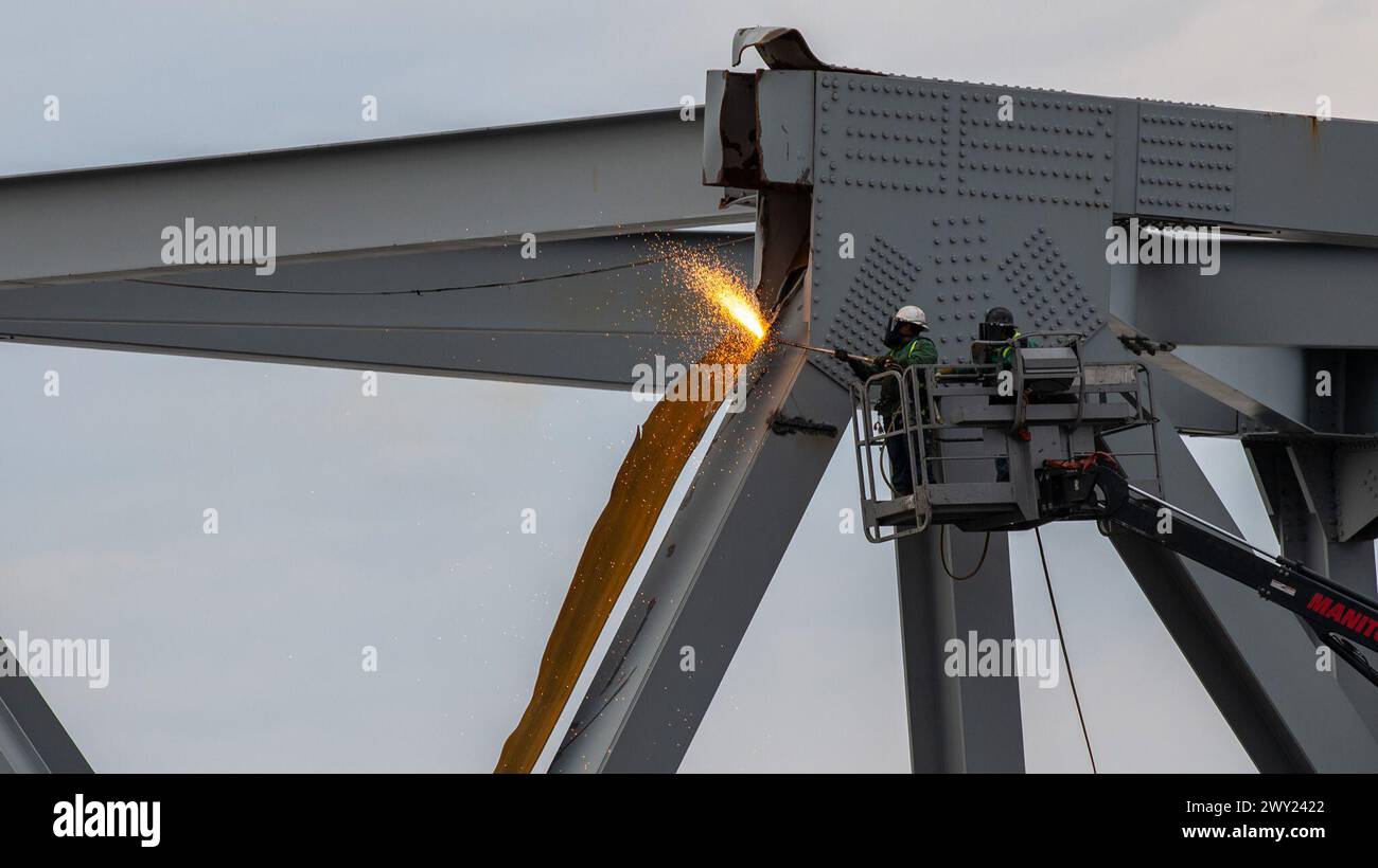 Gli equipaggi di demolizione altamente addestrati iniziarono a tagliare la parte superiore del lato nord del ponte crollato in sezioni più piccole per la rimozione sicura tramite gru nel fiume Patapsco, a Baltimora, Maryland, 30 marzo 2024. Le squadre di recupero utilizzano una torcia da taglio esotermica per separare sistematicamente sezioni del ponte in acciaio, che verrà portata in un sito di smaltimento. (Foto della Guardia Costiera degli Stati Uniti del sottufficiale di terza classe Kimberly Reaves) Foto Stock
