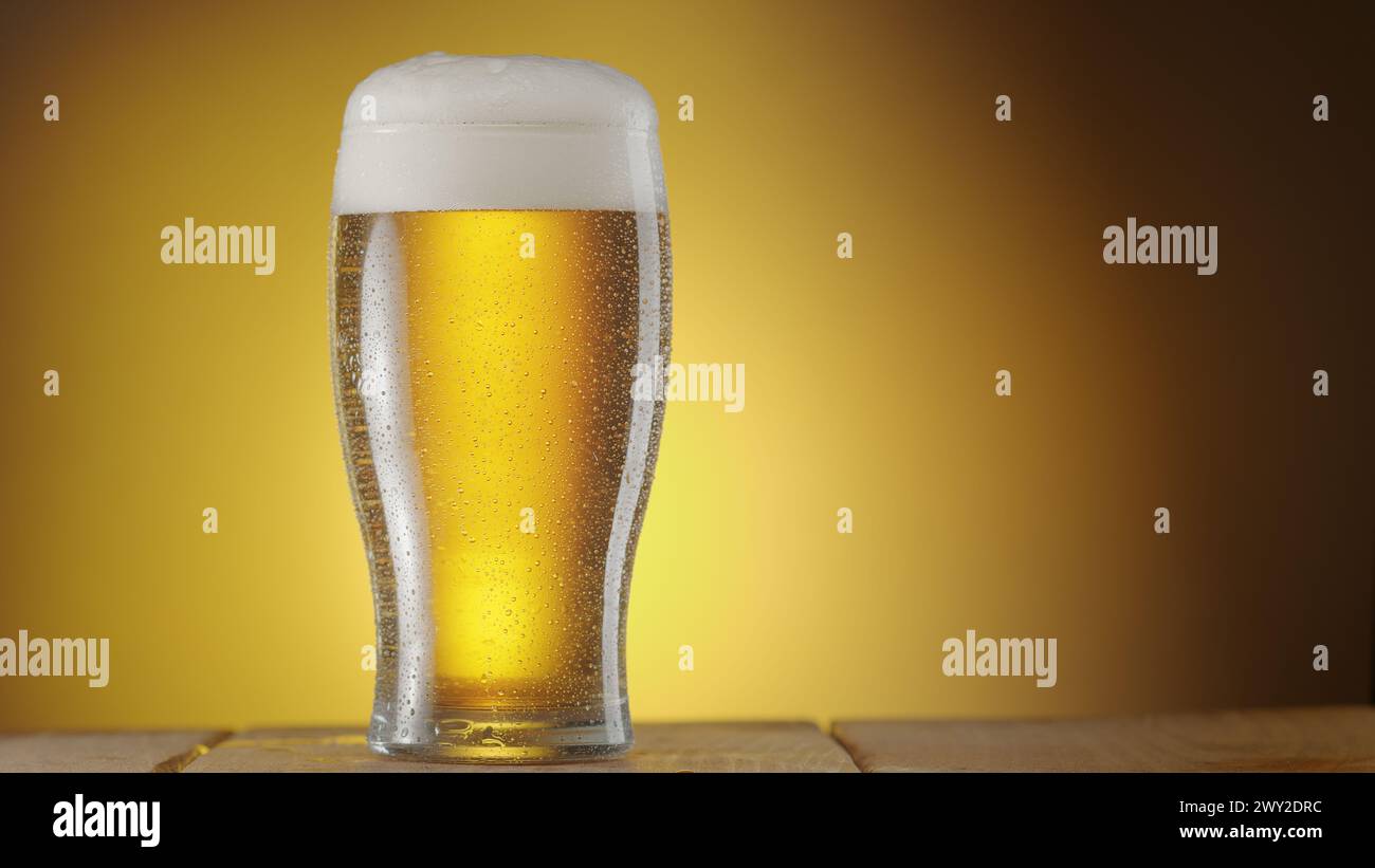 Bicchiere di birra ghiacciata con grande punta di schiuma isolata su sfondo giallo. Foto Stock