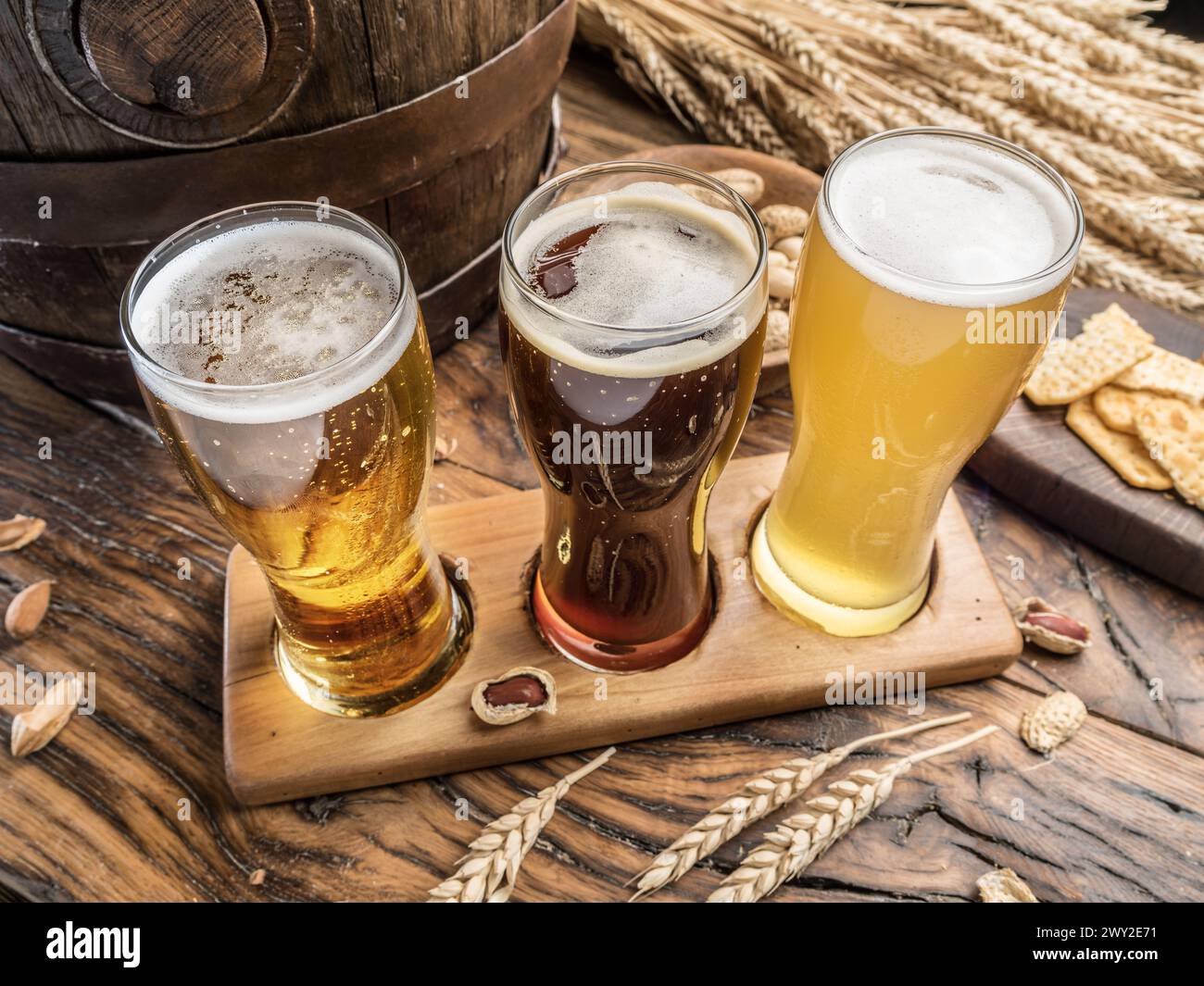 Tre birre artigianali su un volo in legno per la birra. Vista dall'alto di bicchieri da birra, spuntini e botte di birra sullo sfondo. Foto Stock