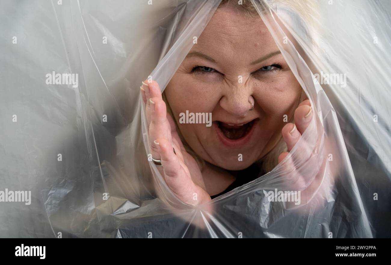 una donna birichina e malvagamente ridendo mette la testa e le mani fuori dalla pellicola di plastica, come una strega di una fiaba, copia spazio Foto Stock