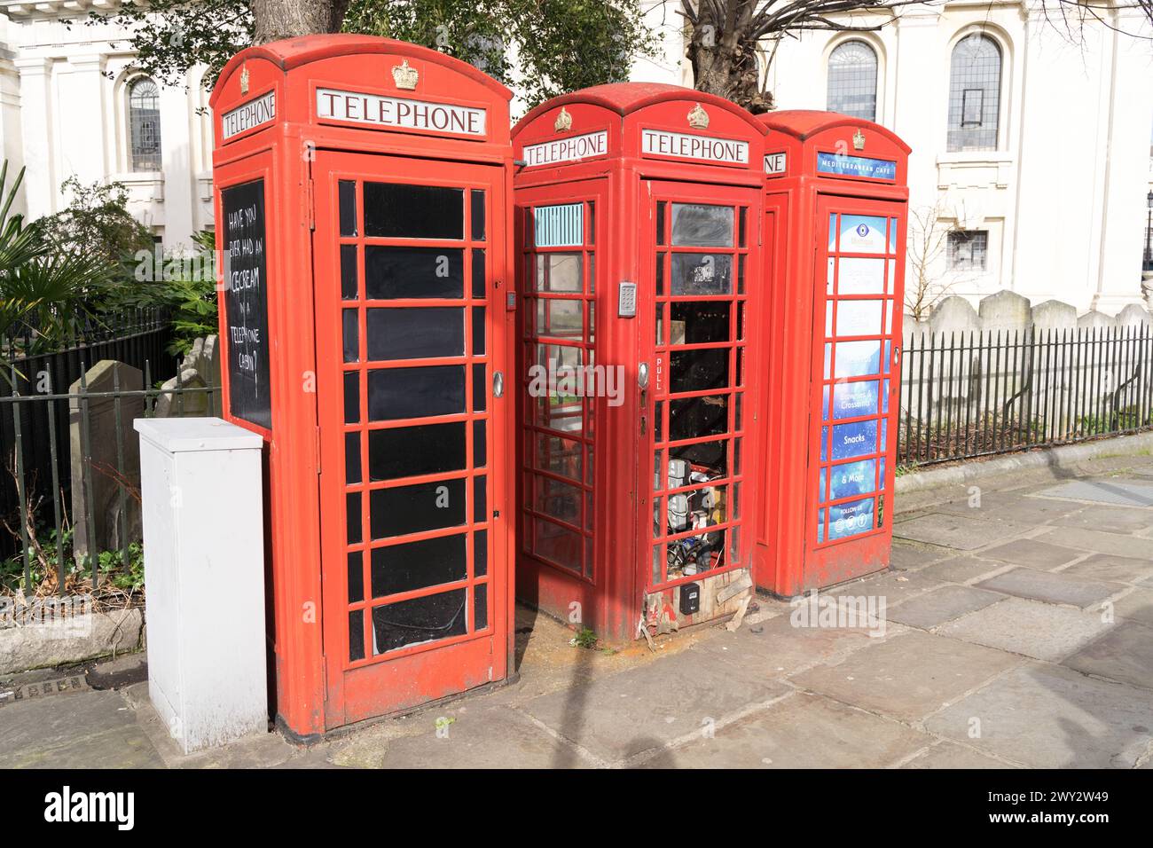 Tre tradizionali cabine telefoniche rosse britanniche che sono state trasformate in chioschi, vetri danneggiati e rotti dei suoi pannelli, costruiti sul marciapiede a Londra nel Regno Unito Foto Stock