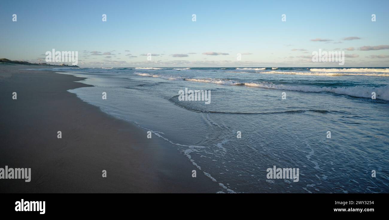 Sunshine Coast, Warana, Kawana che mostra una scena di spiaggia nel tardo pomeriggio con acqua blu scuro, onde bianche da surf e sabbia bagnata sulla costa Foto Stock