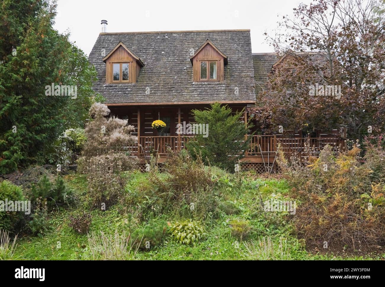 Rustica casa di legno bianca a due piani con lunga veranda e tetto di ciottoli di cedro ricoperto di muschio verde e giardino panoramico con misto Foto Stock