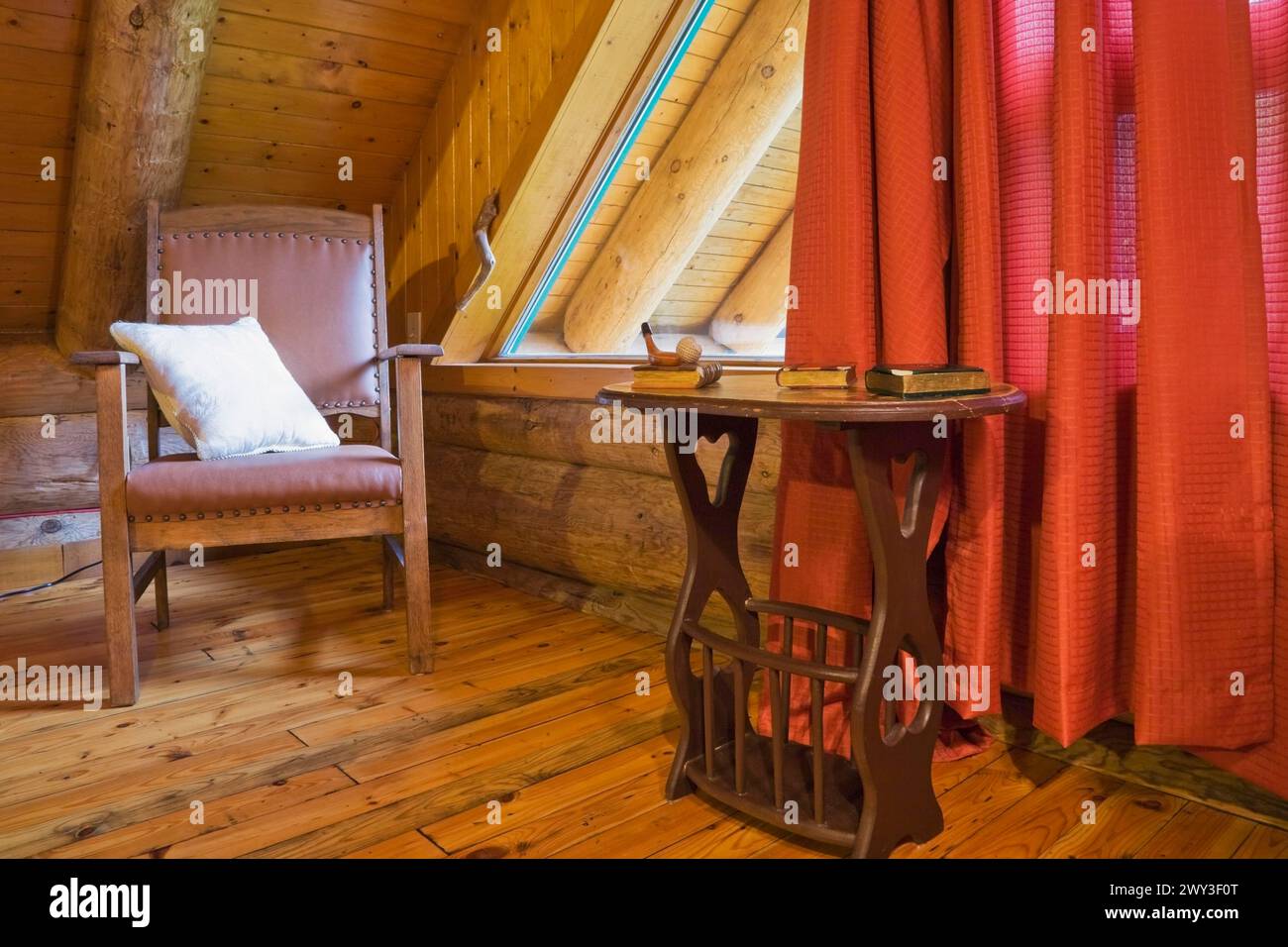 Poltrona in legno marrone con cuscino bianco e tavolino nella camera da letto principale con tende rosse e pavimento in legno al piano superiore all'interno Foto Stock