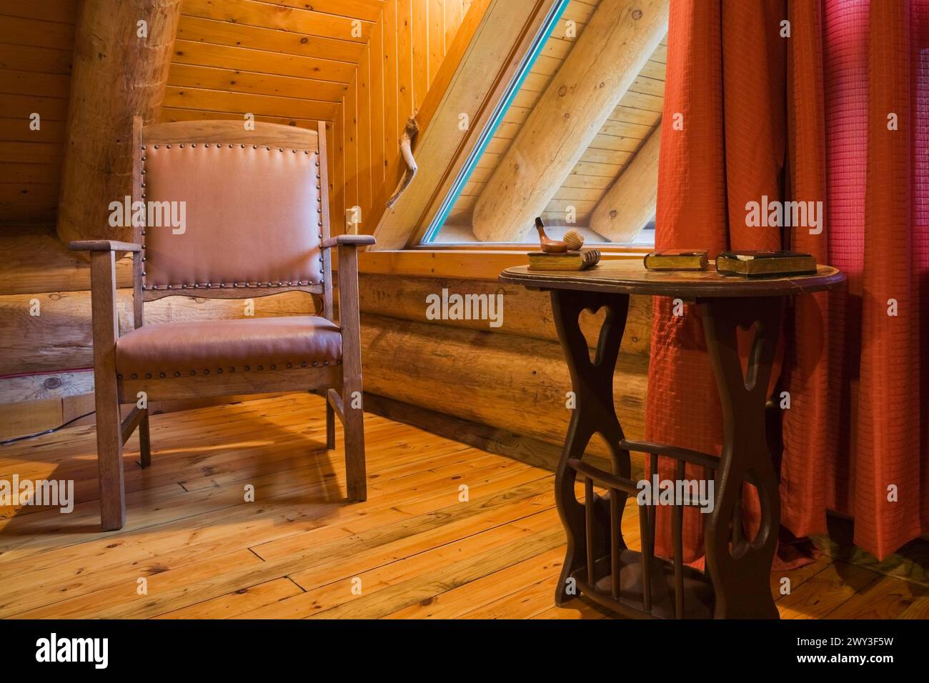Poltrona in pelle di legno marrone e tavolino nella camera da letto principale con tende rosse e pavimento in legno al piano superiore all'interno rustico contemporaneo Foto Stock