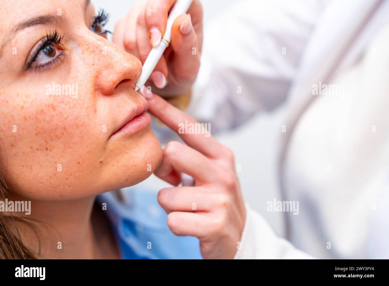 Primo piano delle mani di un cosmetologo che contrassegna i punti per iniettare acido ialuronico sul viso del paziente utilizzando un marcatore in clinica Foto Stock