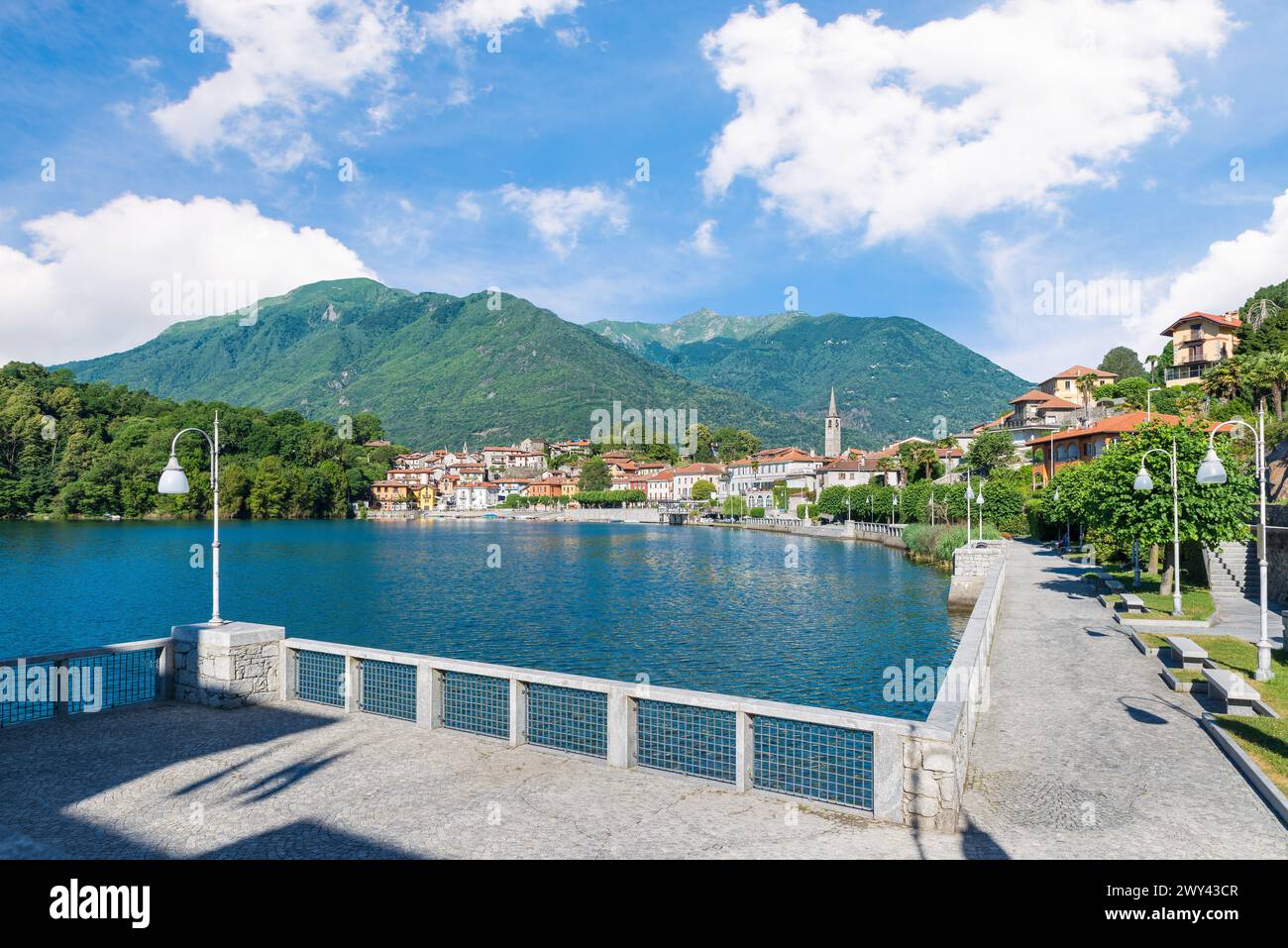 Bellissimo lago italiano tra le montagne. Lago di Mergozzo e città di Mergozzo, Italia. Passeggiata pedonale lungo il lago in estate con cielo azzurro Foto Stock