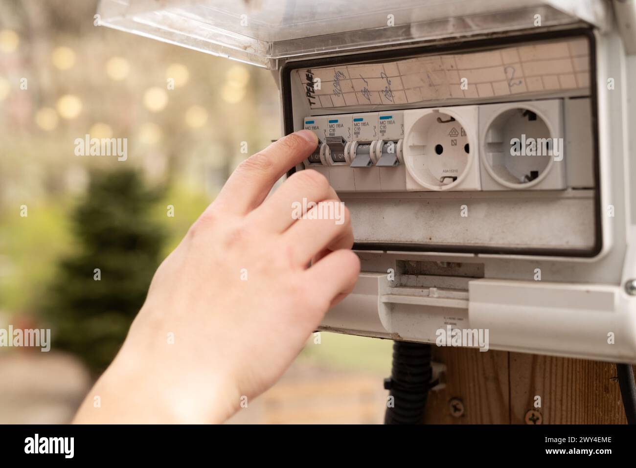 Un dito dell'uomo che controlla l'elettricità nella scatola fusibili all'aperto. Blocco di prese con interruttore in giardino . Foto di alta qualità Foto Stock