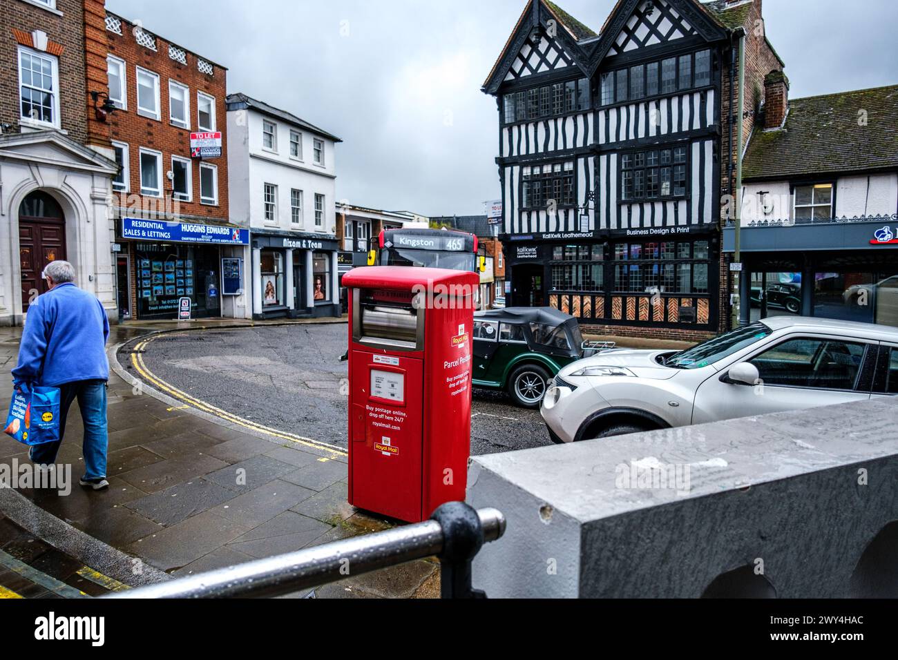 Leatherhead Surrey, Regno Unito, 3 aprile 2024, Woman Carry Shopping Walking Beyond A Royal mail Parcel Post Box in A Wet Day Foto Stock