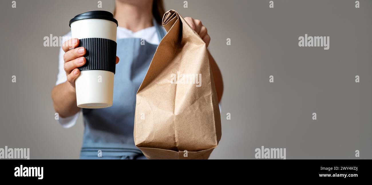 La cameriera ti dà un ordine di cibo da asporto, una tazza da caffè da viaggio e un sacchetto di carta marrone in mano. Foto Stock