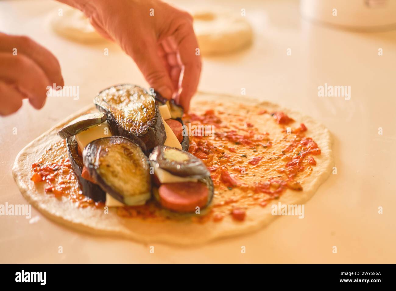 Piatto tradizionale italiano calzone, mani dello chef che aggiungono ingredienti all'impasto della pizza Foto Stock