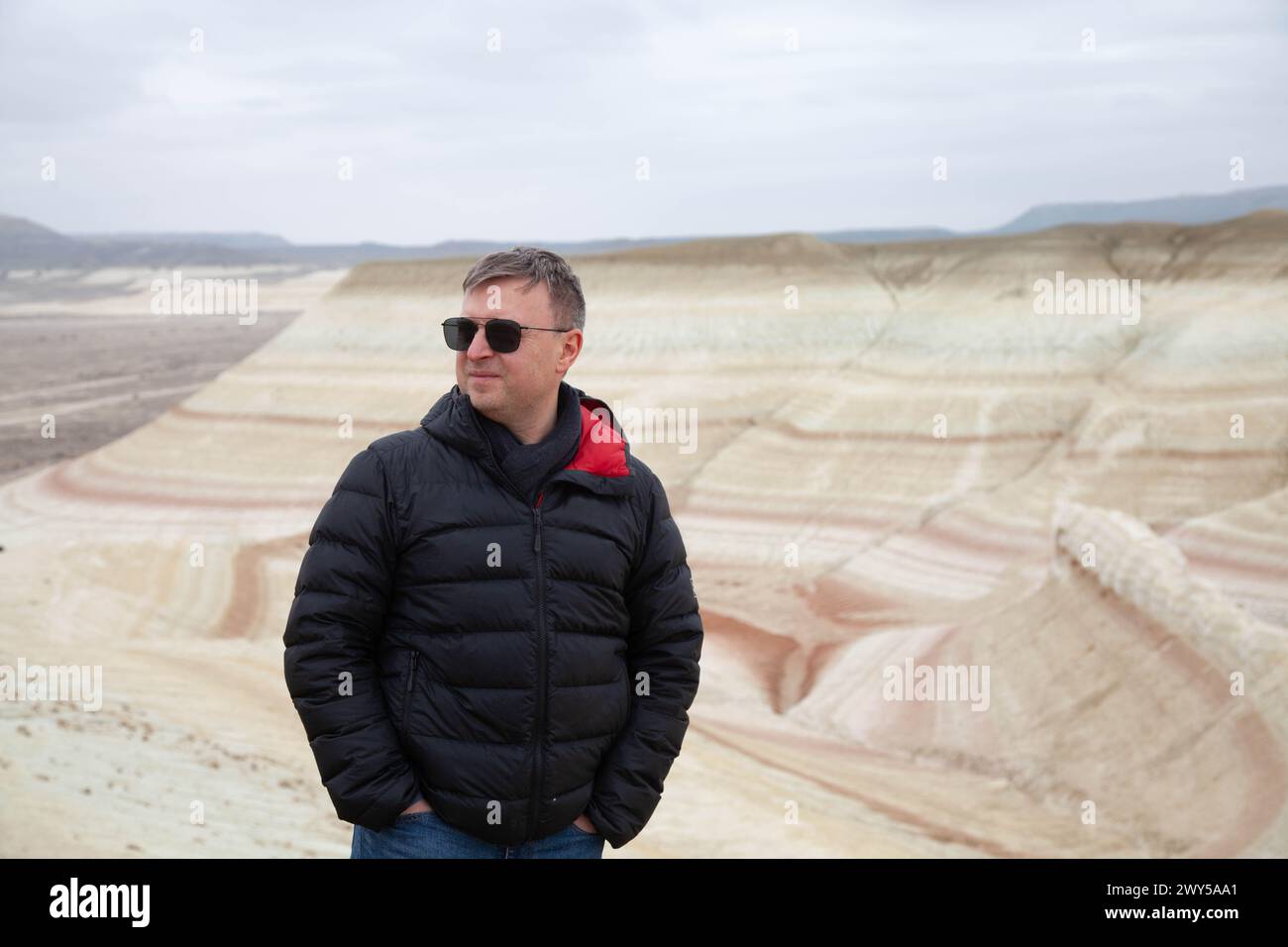 Un uomo con occhiali e una giacca nera si erge davanti alle colline a strisce Tiger, osservando il paesaggio a motivi geometrici. Foto Stock