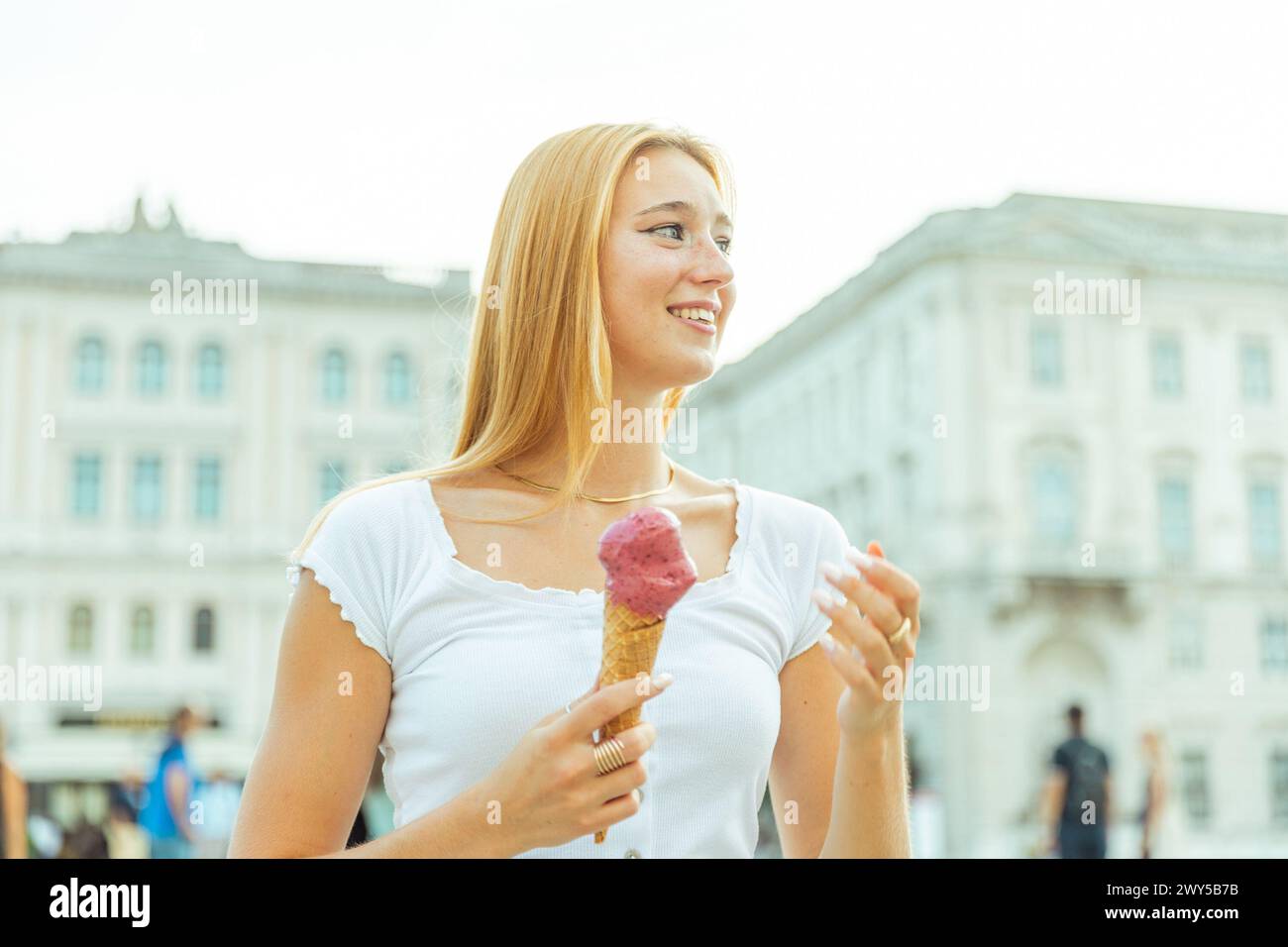 Una giovane donna bianca mangia il gelato ed è felice durante l'estate. Foto Stock