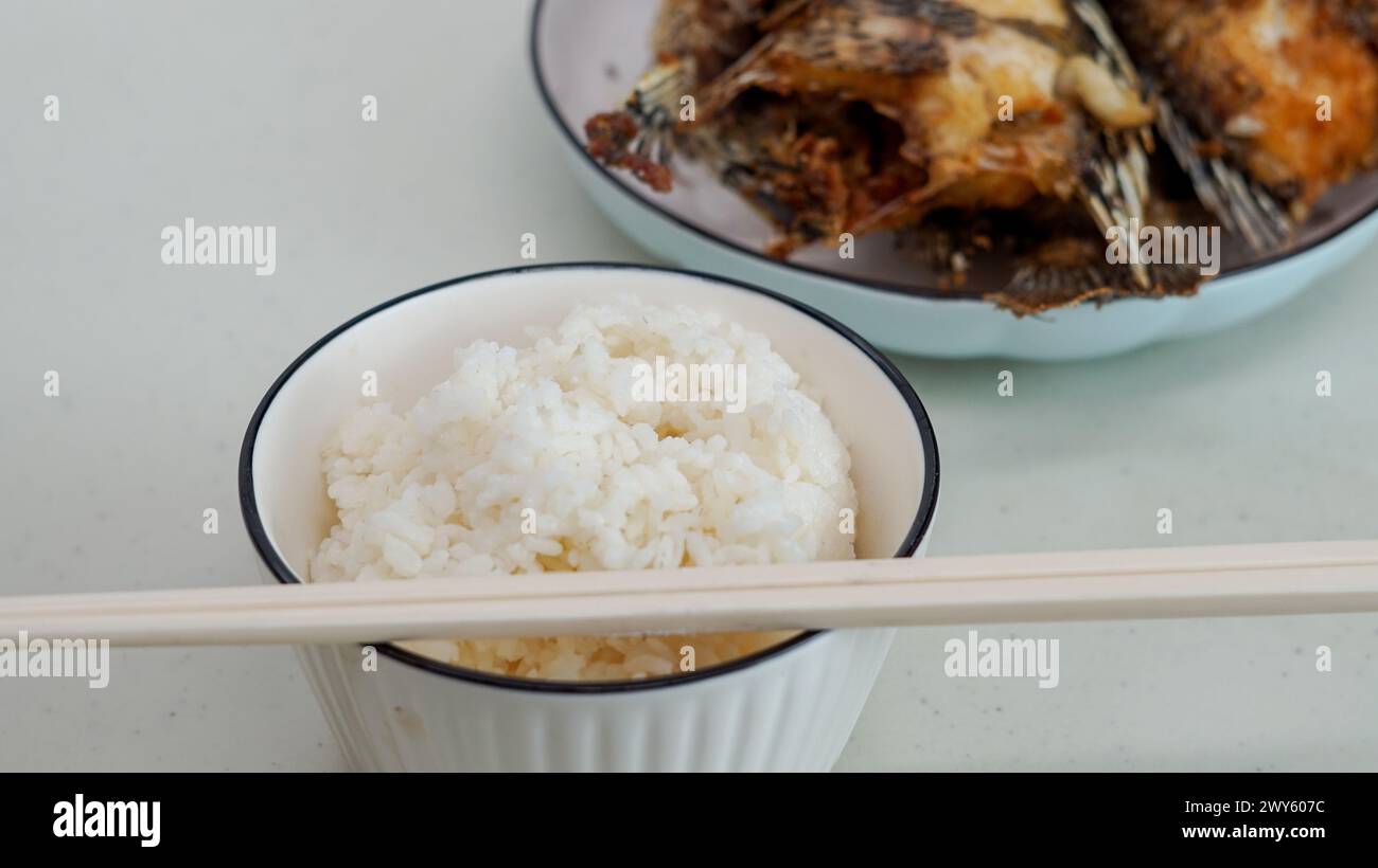 Riso bianco in una ciotola e pesce fritto su un piatto bianco sono serviti sul tavolo Foto Stock