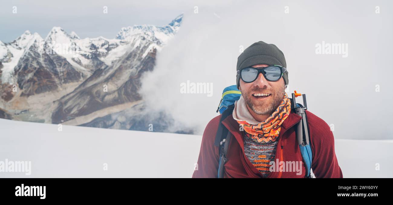 Allegro scalatore ridendo con occhiali da sole ritratto con zaino che sale sulle pendici alte della vetta Mera a 6000 m ammirando il leggendario Monte Everest, Nuptse, Lhot Foto Stock