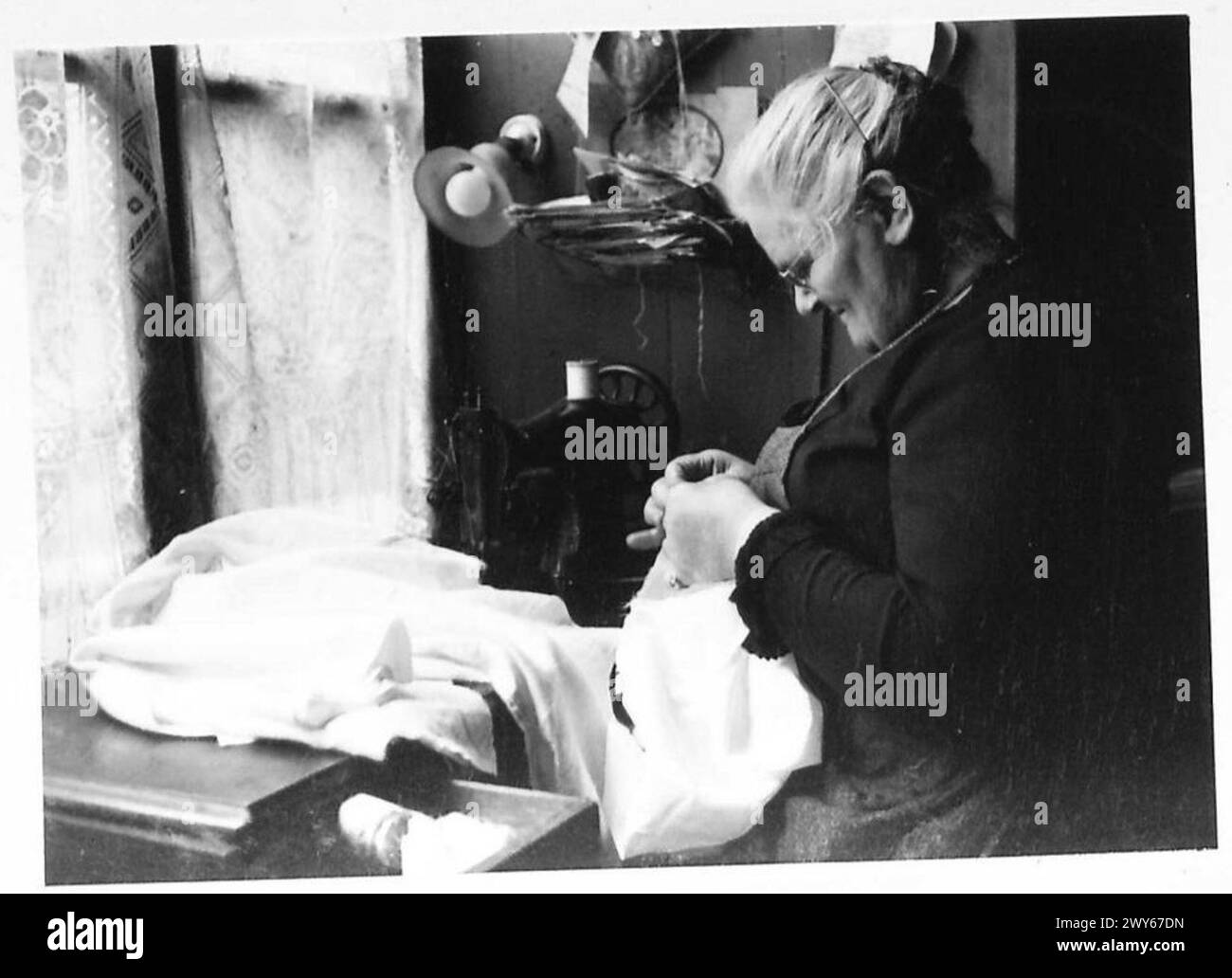 Madame Perine, 61 anni residente a Bayeux, continua il suo lavoro con l'ago mentre stampa un giornale gratuito. Foto Stock