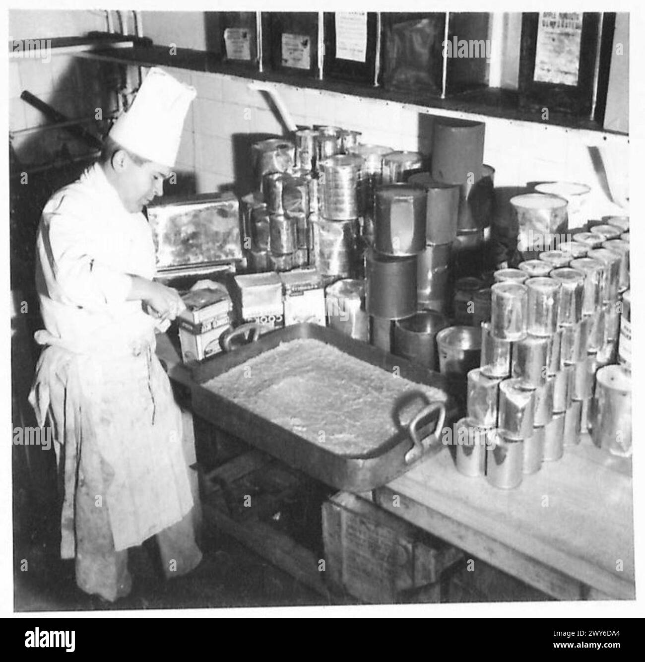 Un cuoco apre barattoli di carne nella sua cucina mentre prepara le razioni dell'esercito durante la guerra. Foto Stock