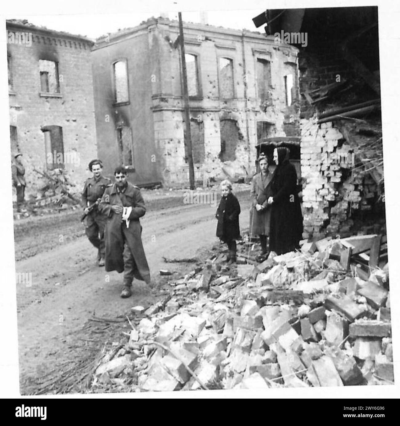 I civili tedeschi osservano che un prigioniero tedesco viene scortato in una gabbia di polizia fuori da un cottage danneggiato da una conchiglia a Brunen, ad est del Reno. Foto Stock