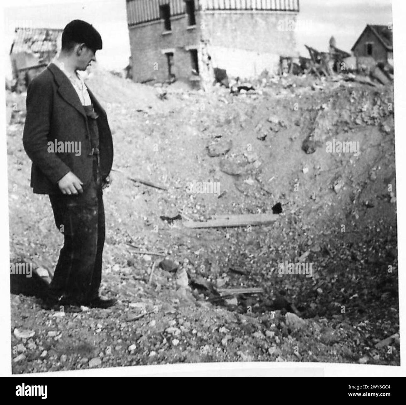 Un civile francese a Caen osserva il cratere che segna la sua casa distrutta durante i bombardamenti, riflettendo l'impatto della guerra sulle aree urbane durante le operazioni dell'esercito britannico, il 21st Army Group. Foto Stock